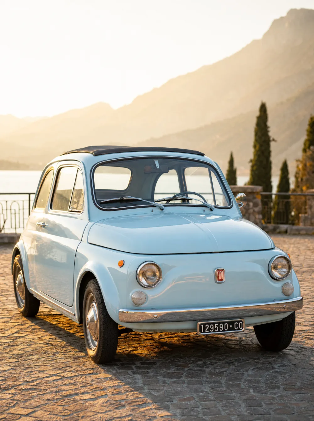 Klassieke Fiat 500 F (Nuova 500) uit 1965 in lichtblauw, driekwart vooraanzicht in gouden ochtendlicht.