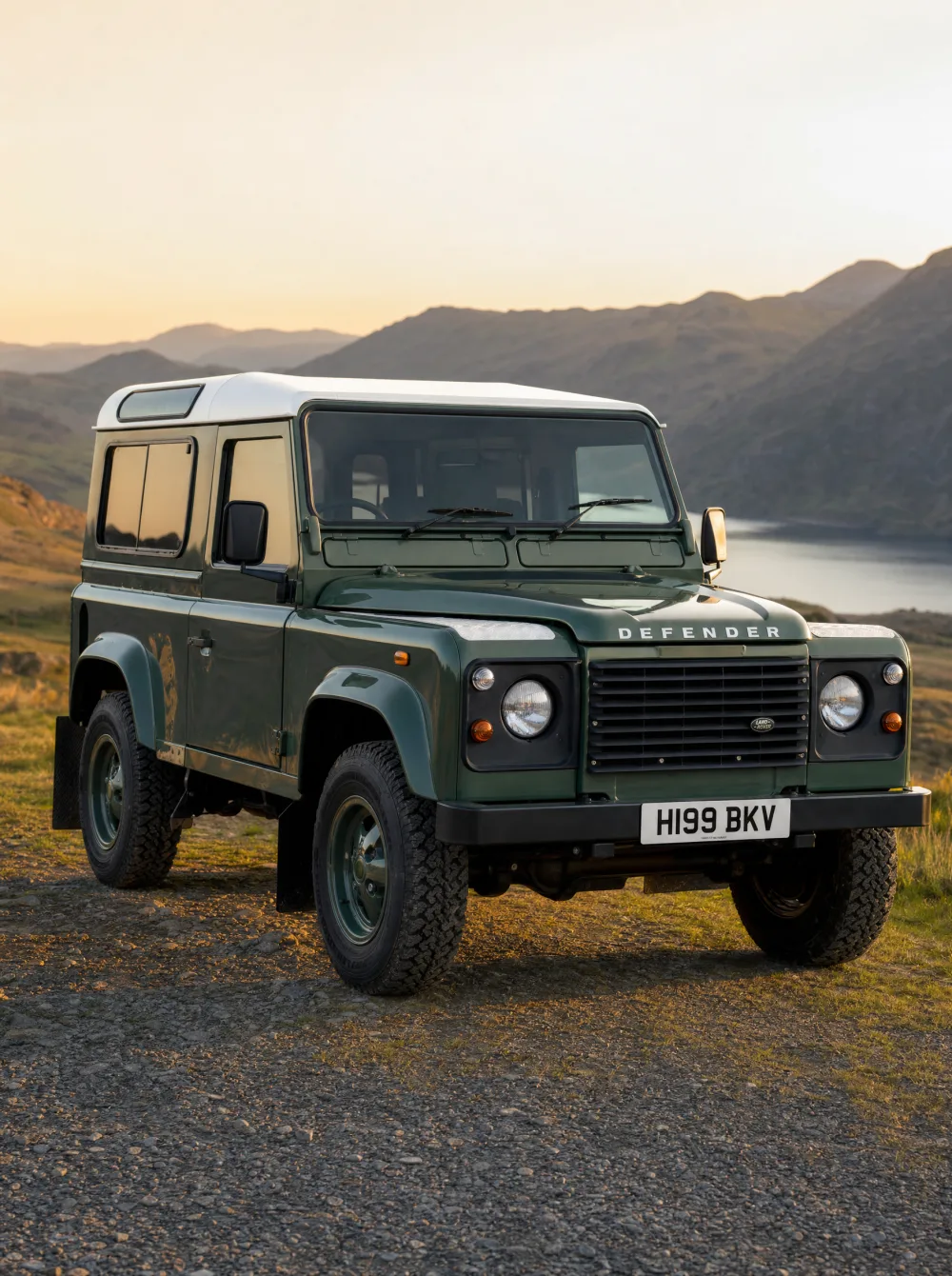 Klassieke Land Rover Defender 90 uit 1990 in Coniston Green, driekwart vooraanzicht in gouden ochtendlicht.