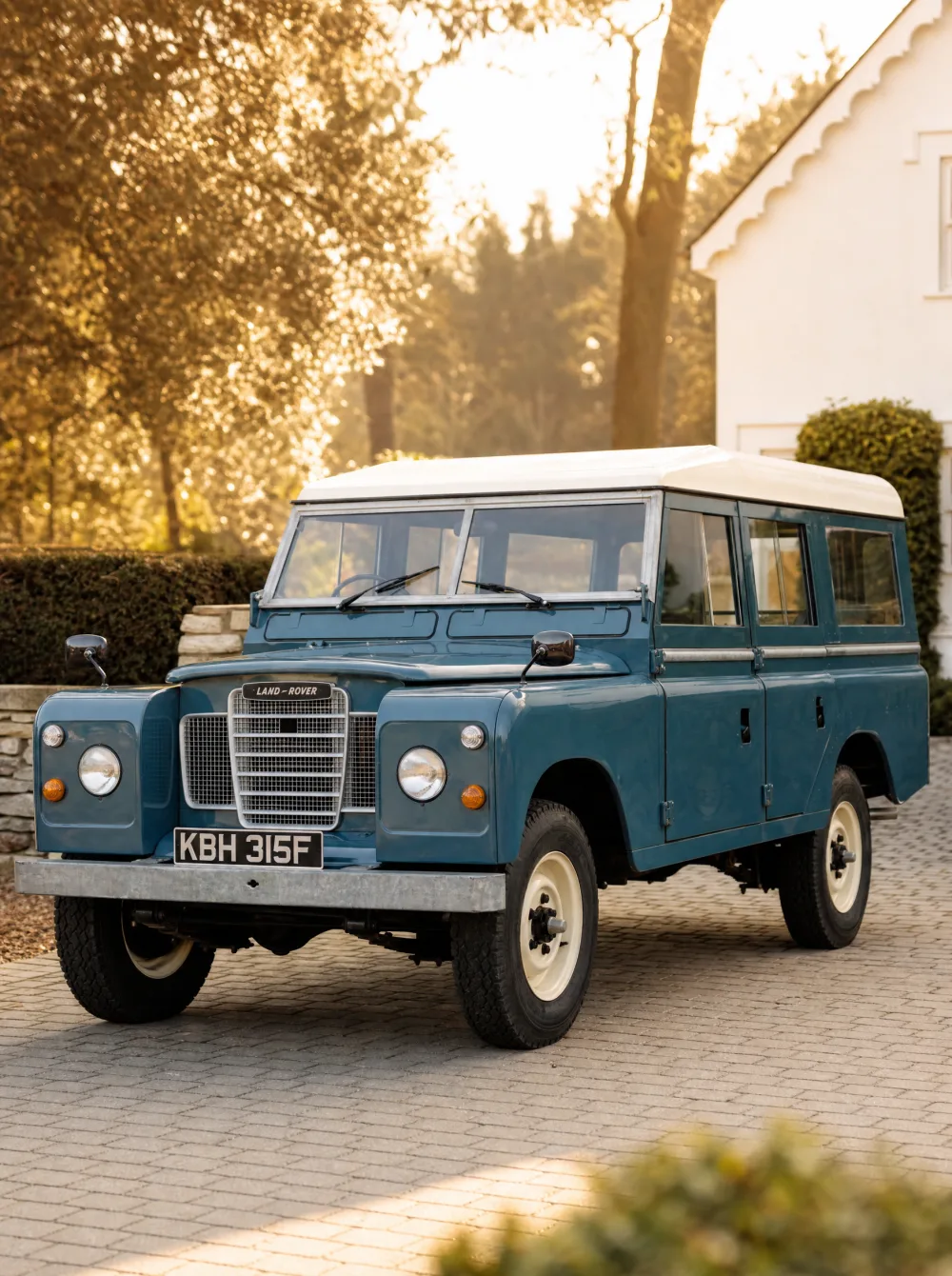 Klassieke Land Rover Series stationwagen uit 1968 in Marineblauw met wit dak, driekwart vooraanzicht in gouden ochtendlicht.